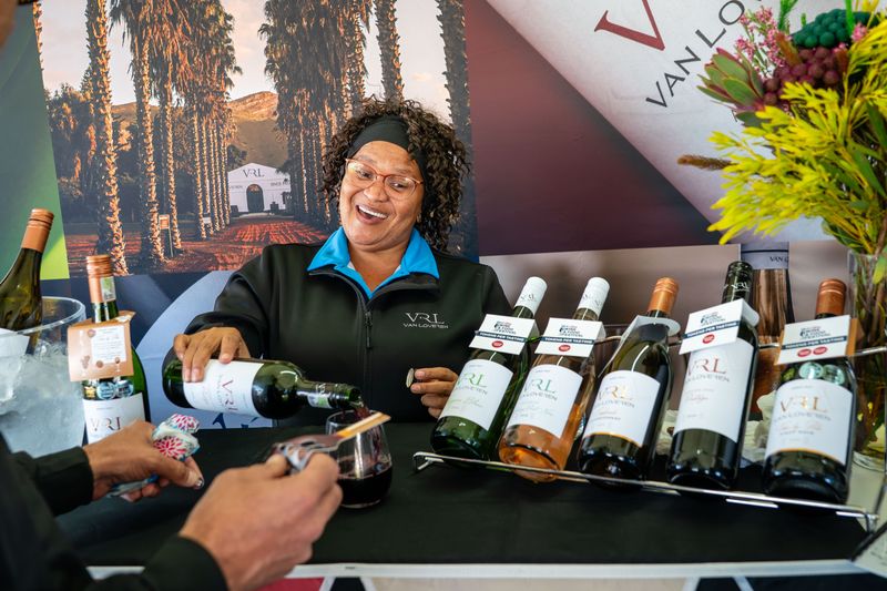 A producer pouring wine at a branded festival stand